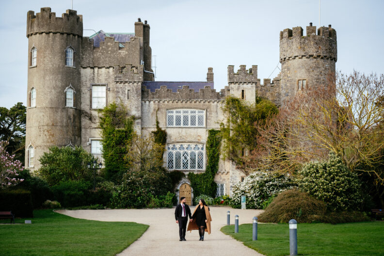 A man and a woman walking down a path in front of a castle.