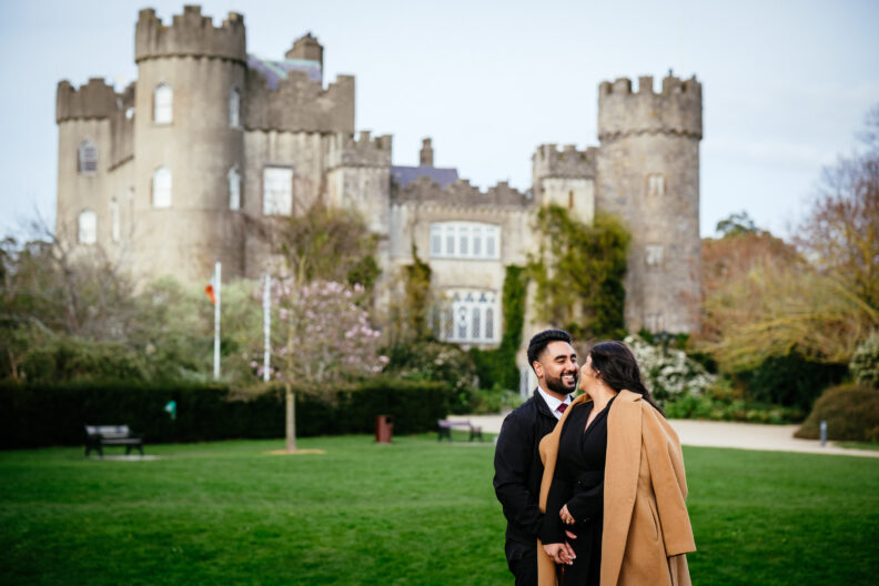 An engaged couple standing in front of a castle.