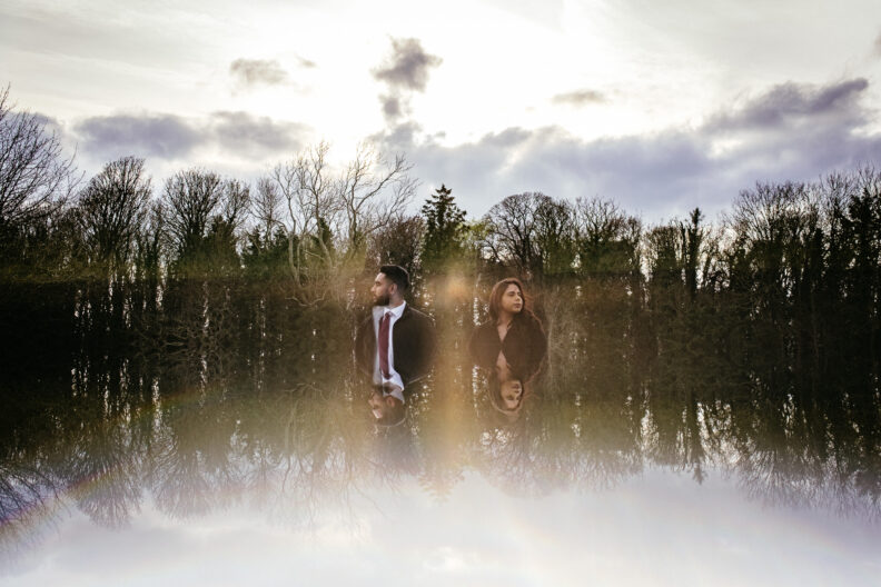 Two people standing in a body of water with trees in the background.