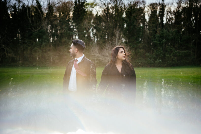 A man and woman standing in a field with a rainbow in the background.