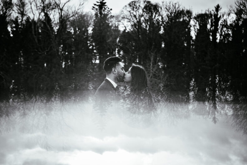 A black and white photo of a couple kissing in the fog.