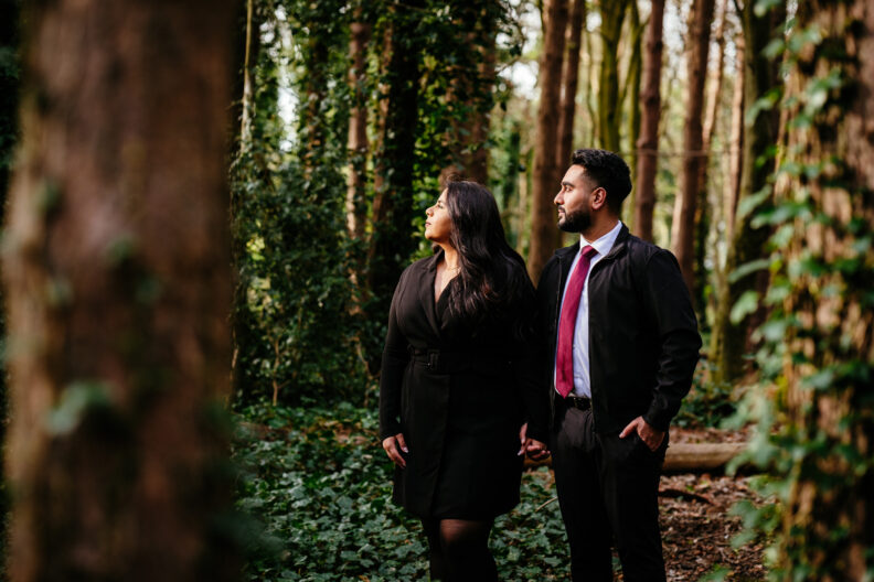An engaged couple standing in a wooded area.