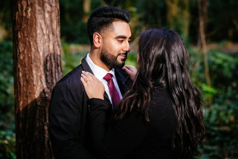 A man and woman hugging in the woods.