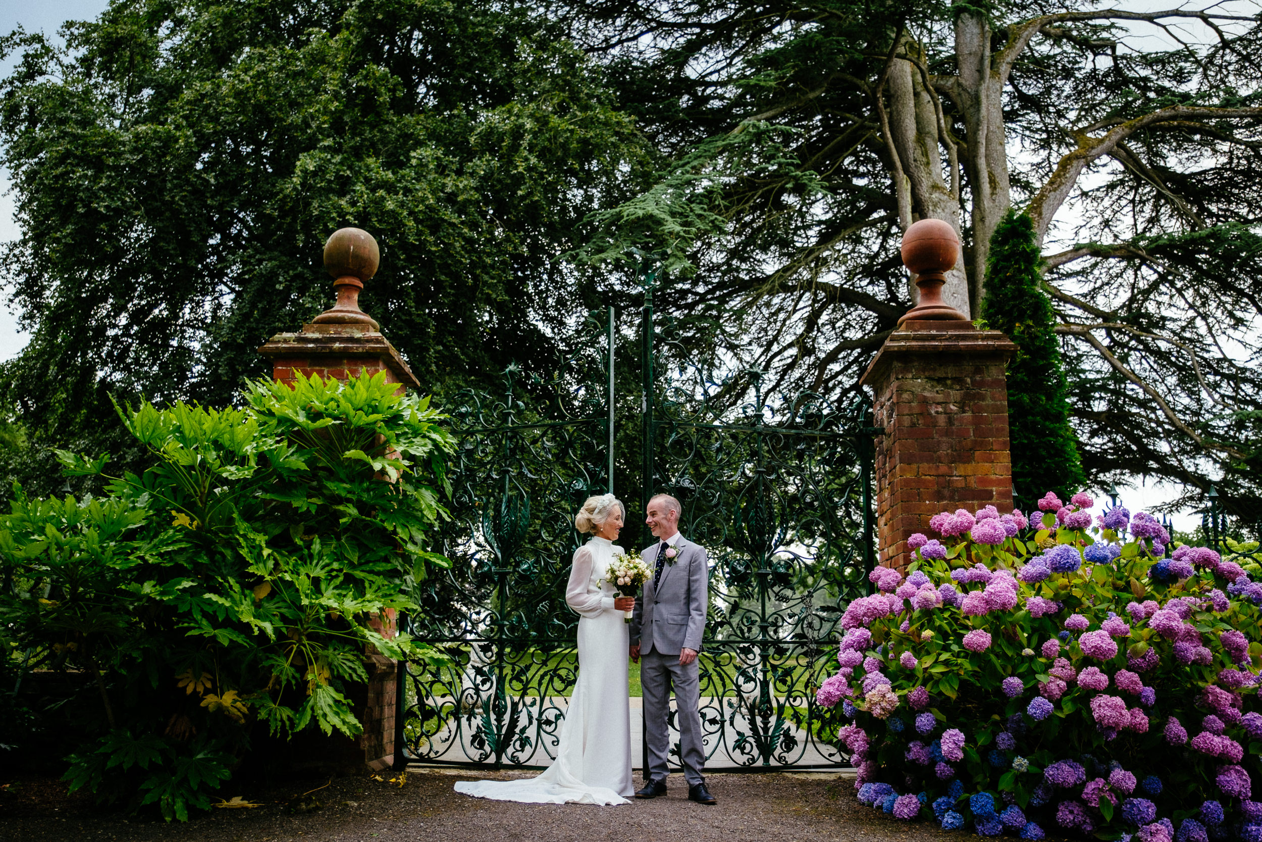 A Summer Wedding at Tankardstown House, with the bride and groom standing in front of a gate in a garden.