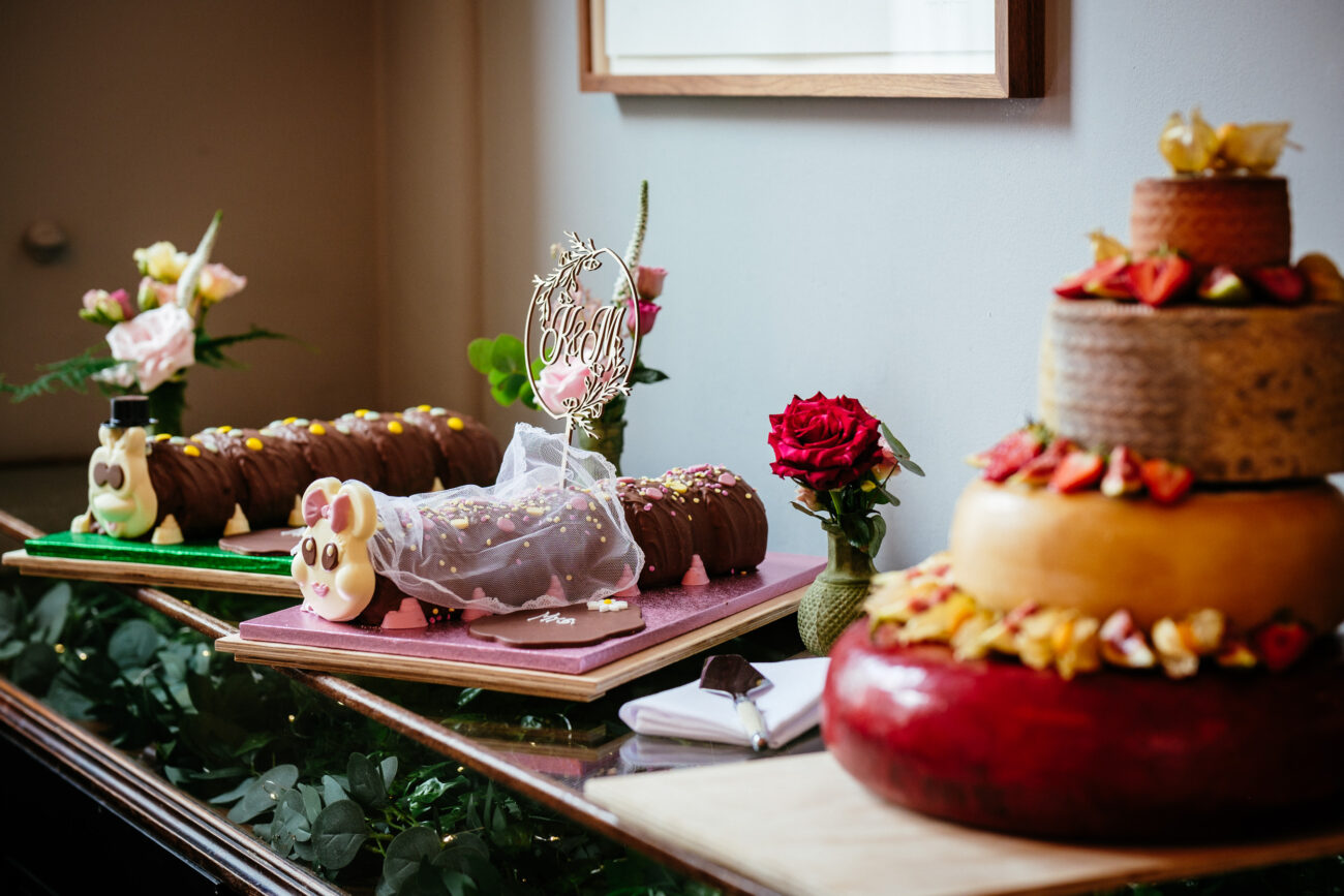 A dessert table featuring a tiered cake with fruit, two character-themed cakes, a "Mr & Mrs" topper, and a red rose in a vase.