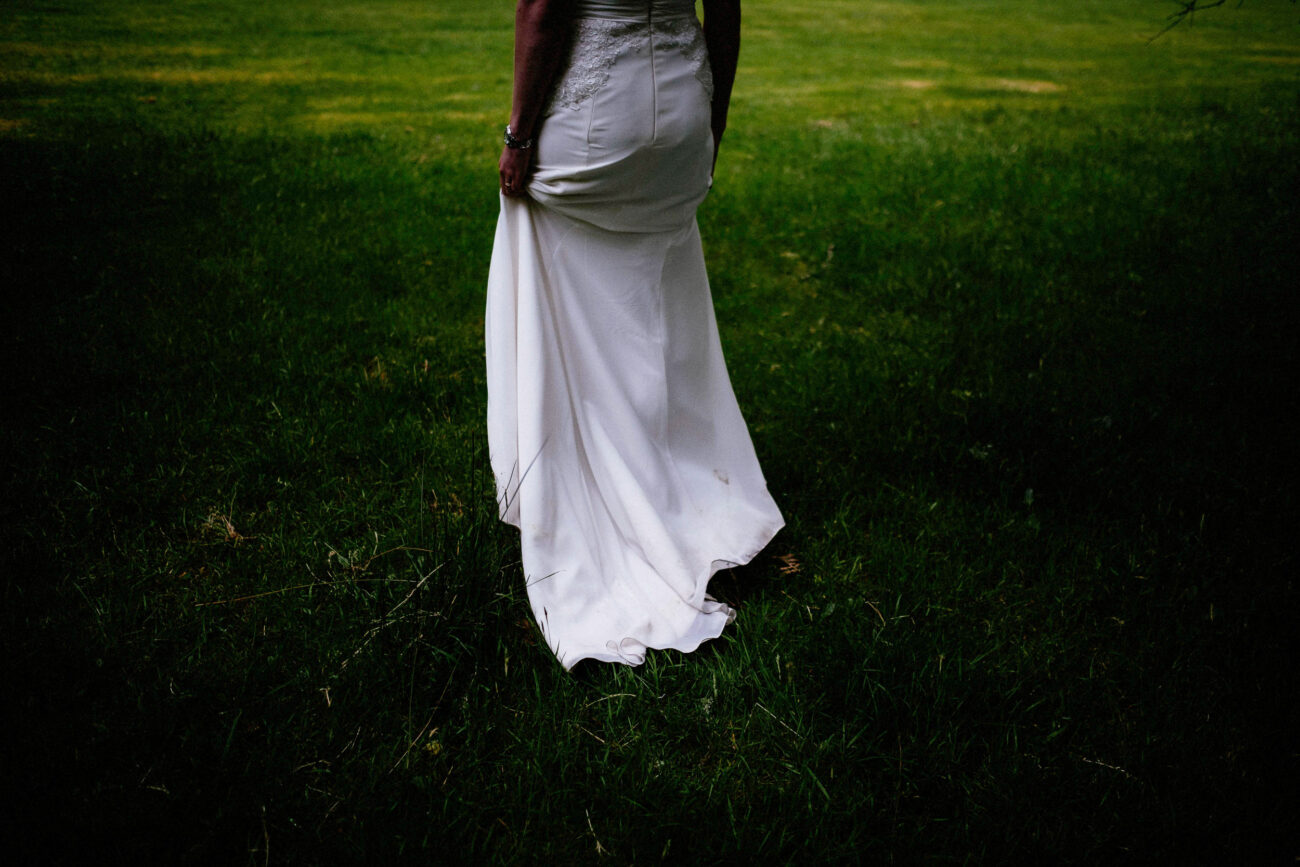 A person in a white dress stands on grass, facing away from the camera.