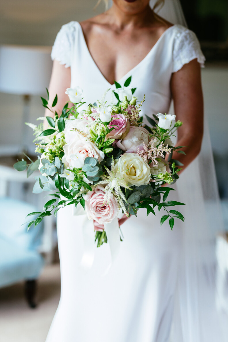 A bride in a white dress holds a bouquet of white and pink flowers with greenery.