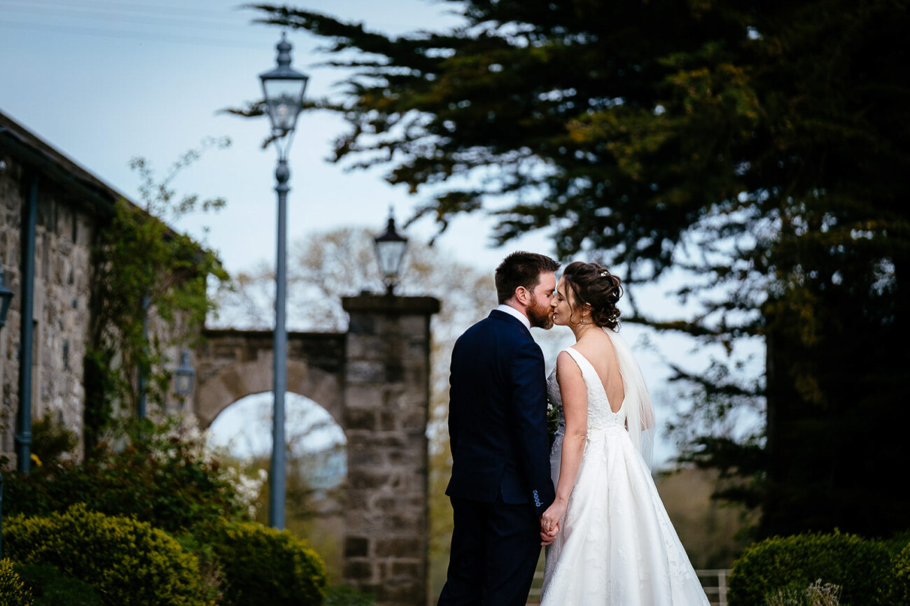 Bride and groom kiss under stone archway in Ballymagarvey Village - Wedding Photographer in Ireland