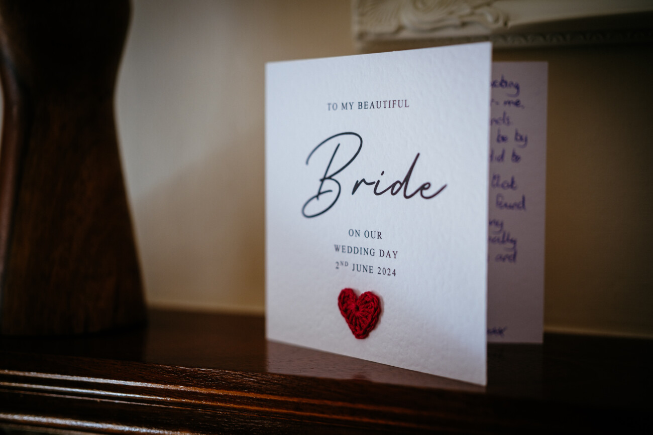 Tara and Darren’s Unforgettable Wedding at Bellingham Castle 38 A white wedding card for a bride with black text and a red heart sits on a wooden surface, dated 2 June 2024, celebrating a beautiful wedding at Bellingham Castle.