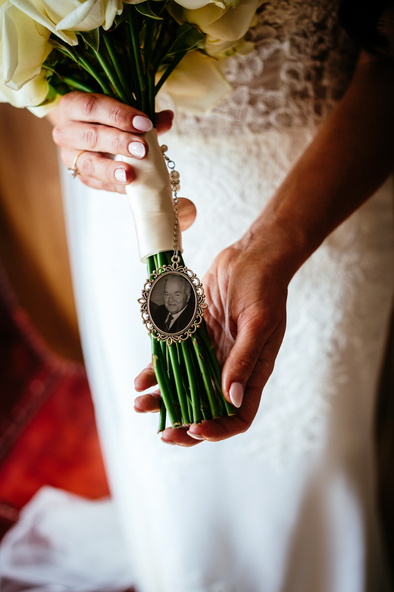 Tara and Darren’s Unforgettable Wedding at Bellingham Castle 42 A bride at her wedding at Bellingham Castle holds a bouquet wrapped with a ribbon and a decorative photo charm featuring a black-and-white portrait.