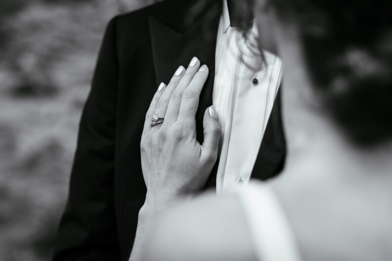 A close-up, black-and-white photo captures a hand with a ring resting on another person’s chest in a suit and bow tie—a timeless moment perfect for Secret Proposals & Elopements in Ireland.