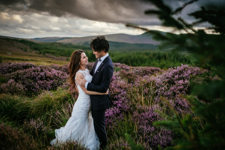 Elope in Ireland: A Simple, No-Stress Guide 31 A bride and groom stand embracing in a field of purple heather, with rolling hills and a cloudy sky in the background—capturing a timeless moment of wedding photography as they elope in Ireland.