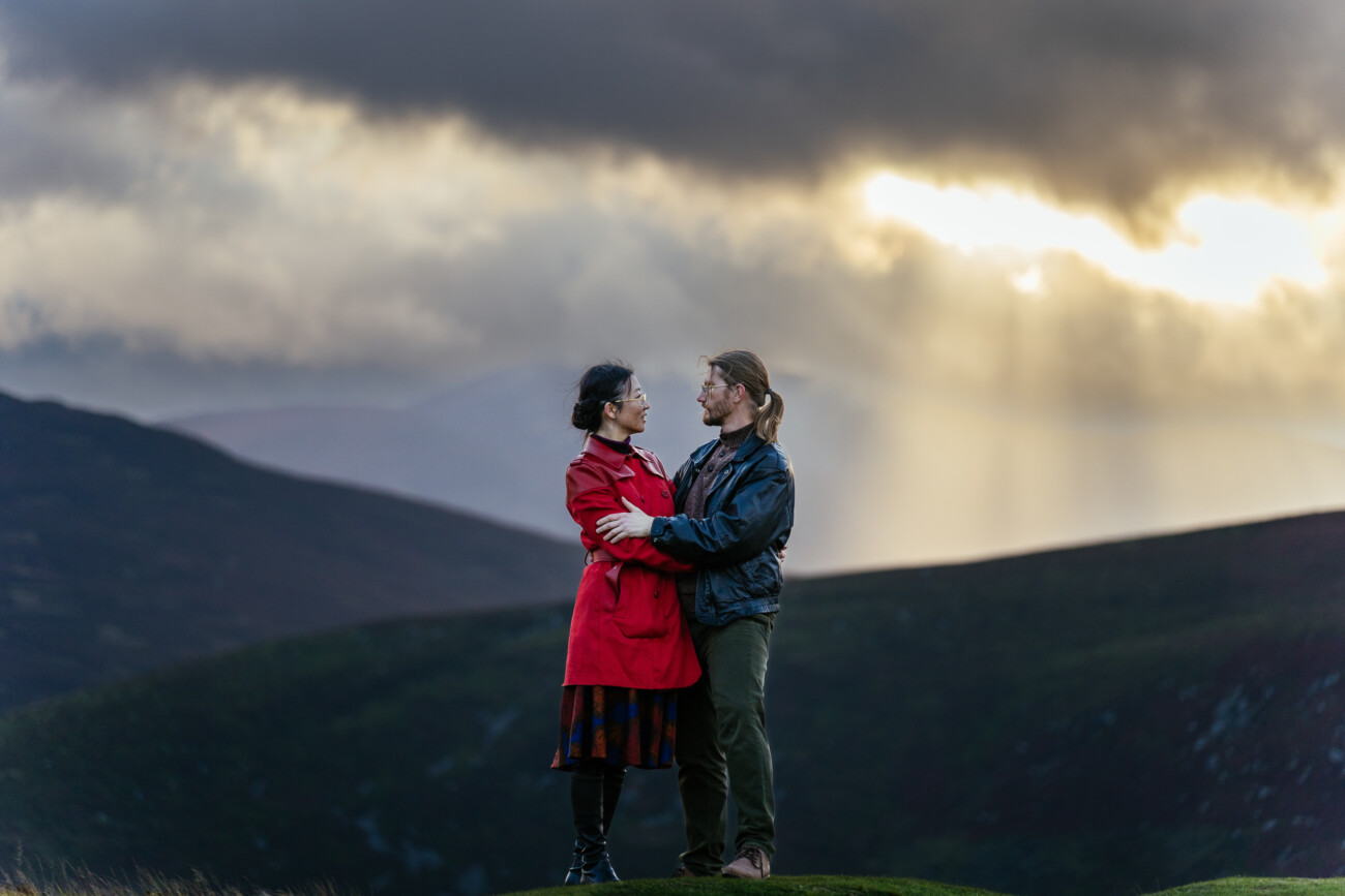 A couple on a grassy hill with dramatic Irish skies behind them