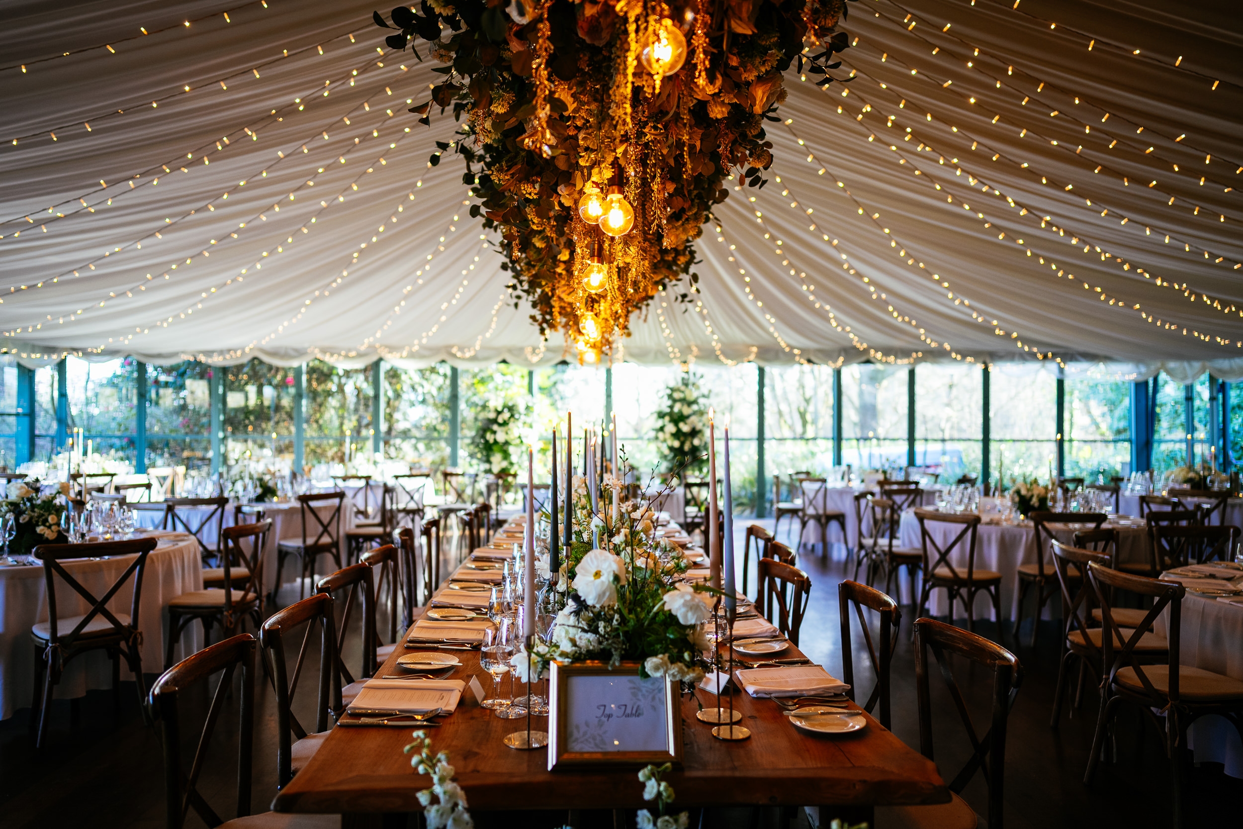 A decorated banquet hall at Virginia Park Lodge with long tables set for a wedding, floral centerpieces, and string lights hanging from the ceiling.