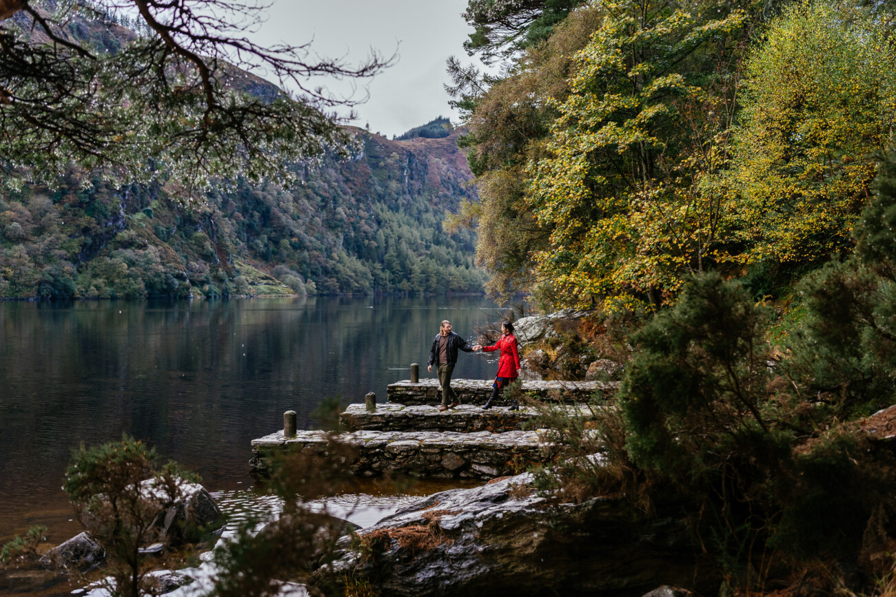 A woman in a vibrant red jacket and her husband walking through the misty Wicklow Mountains with the Irish landscape in the background.