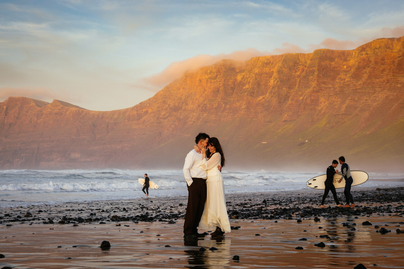 A couple embrace on a rocky beach at sunset for a destination wedding