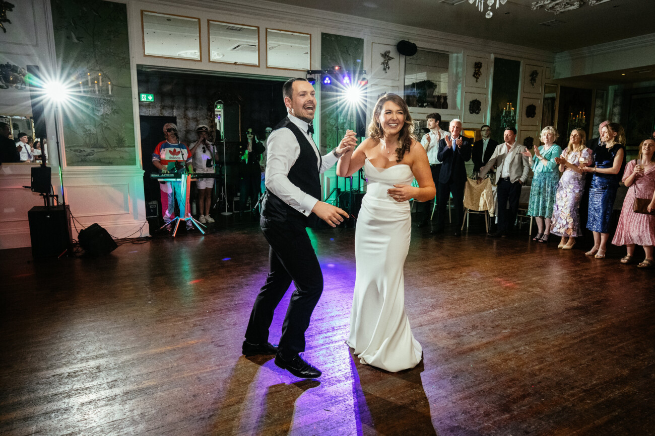 A bride and groom dance in a brightly lit reception hall as guests watch and smile from the sidelines, capturing a timeless moment reminiscent of Castle Durrow Wedding Photography.