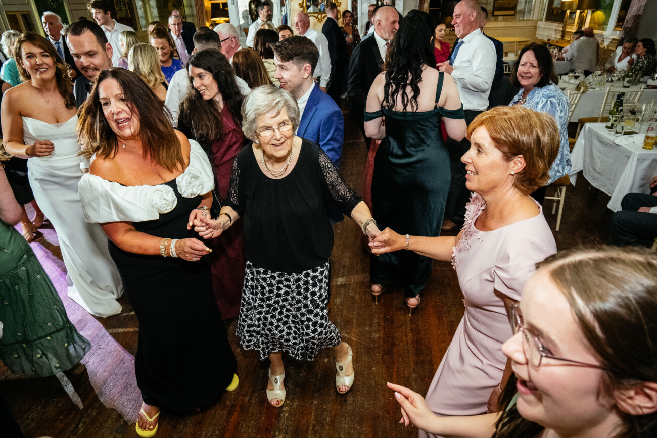 A group of people of various ages holding hands and dancing together at an indoor celebration, beautifully captured by Castle Durrow Wedding Photography.