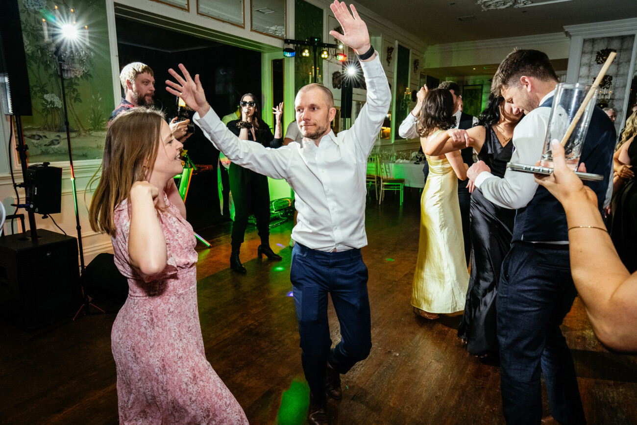People dance energetically on a wooden floor at an indoor event, with green stage lights and party décor in the background, capturing the lively atmosphere typical of Castle Durrow Wedding Photography.