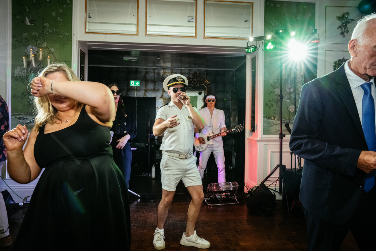 A man in a white naval uniform sings into a microphone as a band plays. People dance and interact on the crowded indoor stage with colourful lighting, capturing the vibrant energy perfect for Castle Durrow Wedding Photography.