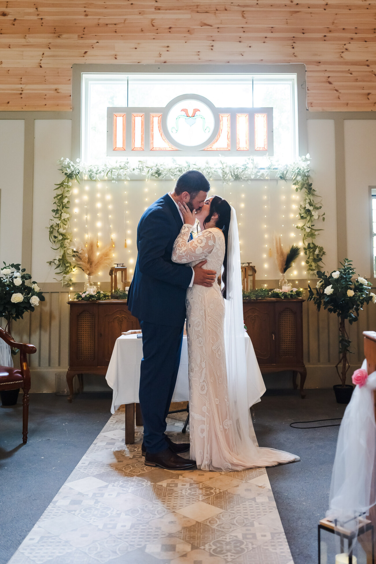 A Relaxed Summer Wedding at Village Barn, Tyrellspass | Amy & Eoghan 43 A bride and groom kiss at the altar in a decorated church during their wedding ceremony.