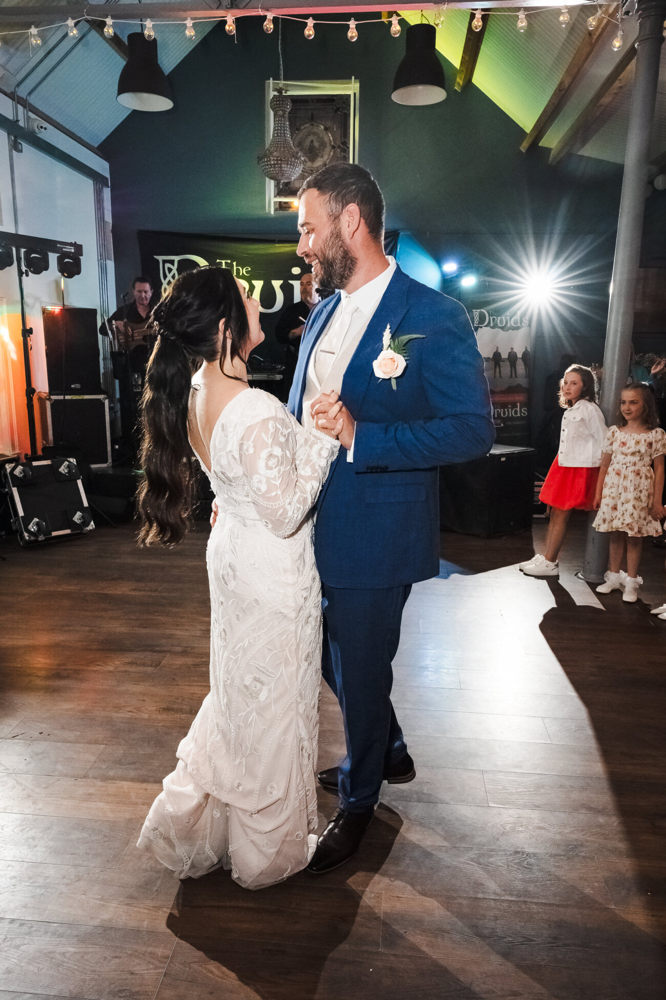 A Relaxed Summer Wedding at Village Barn, Tyrellspass | Amy & Eoghan 107 A bride and groom dance together at their wedding reception, smiling at one another, while guests and children watch in the background.