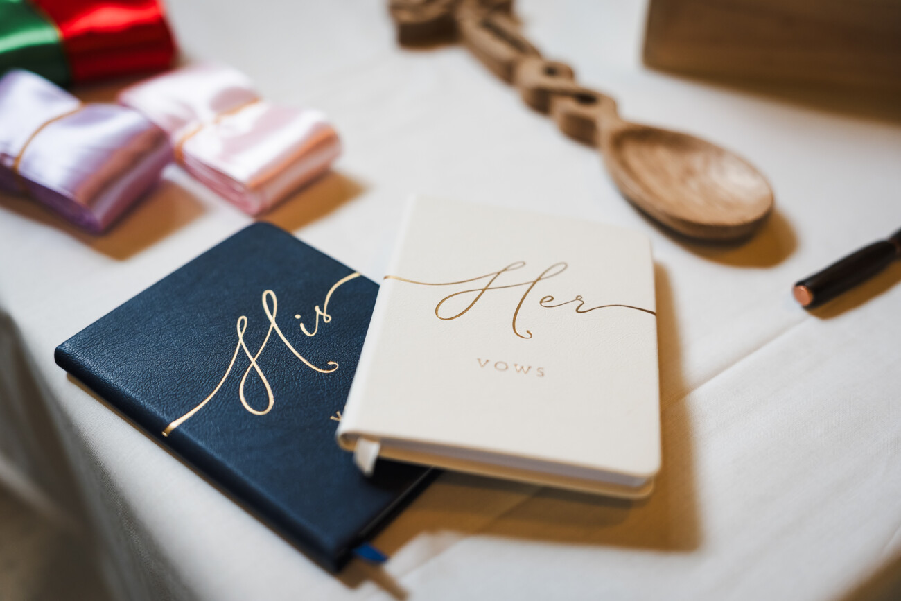 A Relaxed Summer Wedding at Village Barn, Tyrellspass | Amy & Eoghan 9 Two vow books labelled “His” and “Her” rest on a table with wooden utensils, ribbon bundles, and a pen nearby.