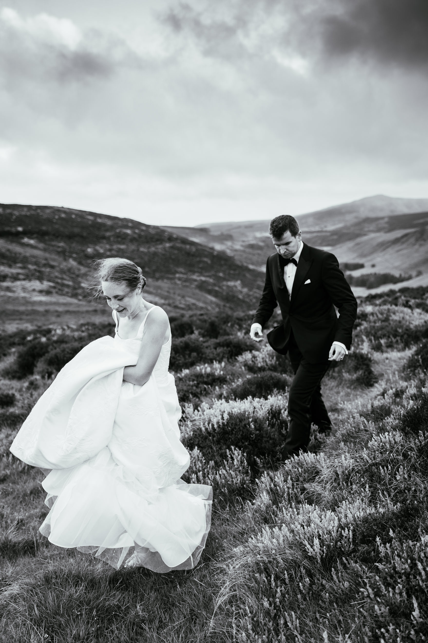 Planning a Causeway Coast Elopement 2 A bride and groom walking through a grassy, hilly landscape on the Causeway Coast, the bride holding her dress as she walks
