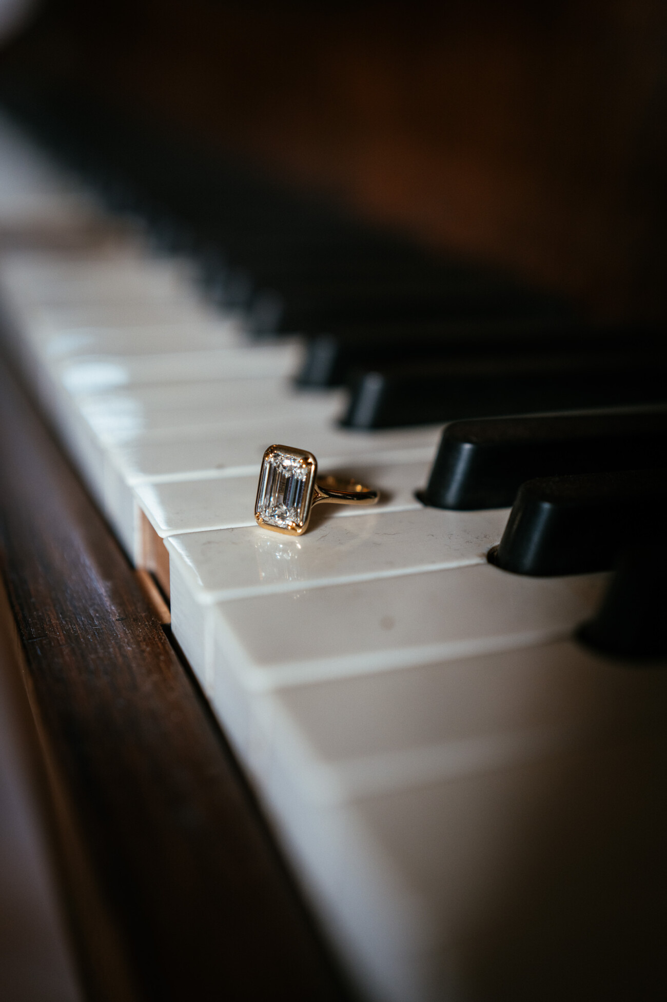 A Secret Proposal at Howth Cliffs & a Private Hour at Howth Castle: Joseph & Shannon's Engagement Shoot 30 A gold ring with a rectangular clear gemstone rests on a white piano key, with black keys and part of the wooden piano visible in the background.